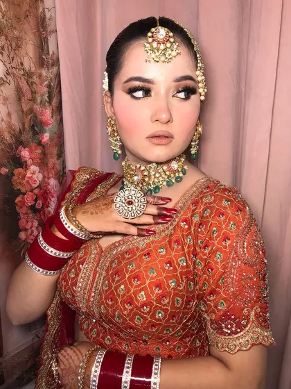 This bride's look is all about the eyes and the jewelry. Her orange-red lehenga is paired with a stunning kundan and emerald set.