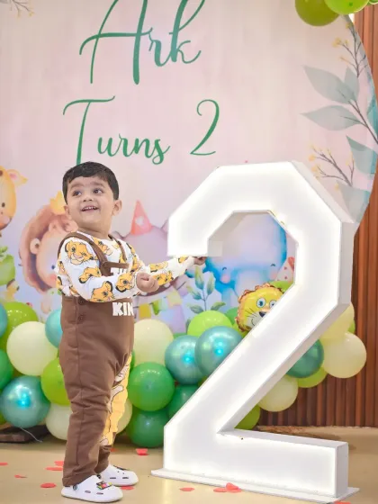 A happy toddler poses next to a large, illuminated number '2' at his jungle-themed birthday party. We make sure to get great solo portraits of the birthday boy or girl with their unique party decorations.
