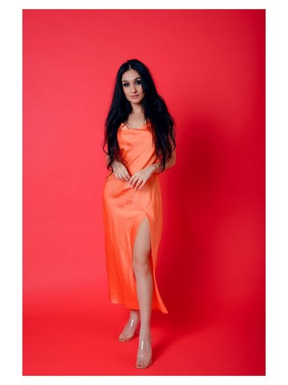 A full-length shot of a model in a vibrant orange slip dress against a bright red background. The color combination is bold and eye-catching, perfect for a brand that wants to stand out.