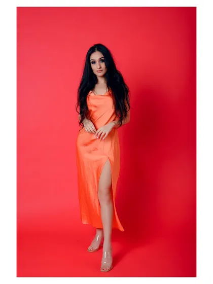 A full-length shot of a model in a vibrant orange slip dress against a bright red background. The color combination is bold and eye-catching, perfect for a brand that wants to stand out.