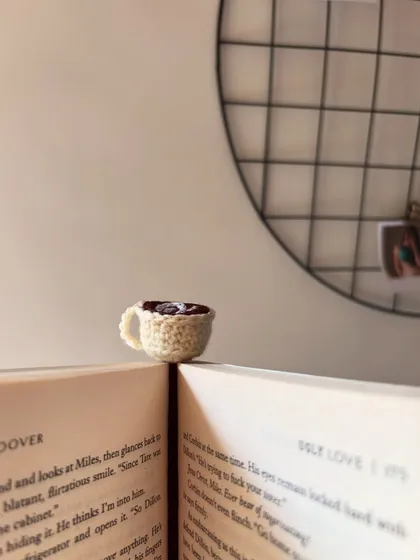 The tiny coffee cup bookmark sitting on the edge of an open book.