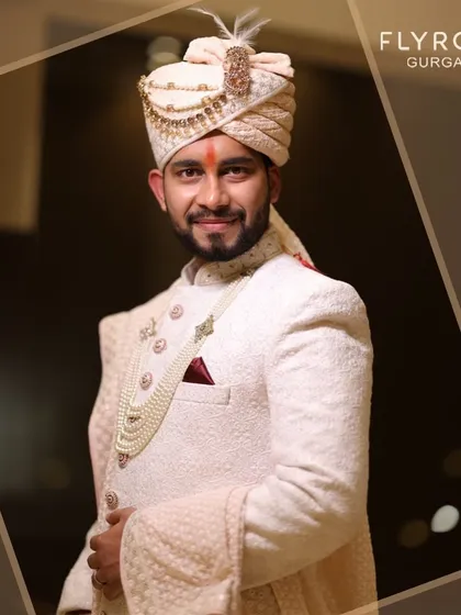 A close-up of a groom looking sharp and ready for his big day. He's wearing an elegant off-white sherwani with a matching safa and a pearl mala, a classic choice for wedding ceremonies.