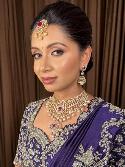A sophisticated look for an evening event. The makeup features a subtle smokey eye and a neutral lip, complementing her deep purple saree and diamond jewelry.