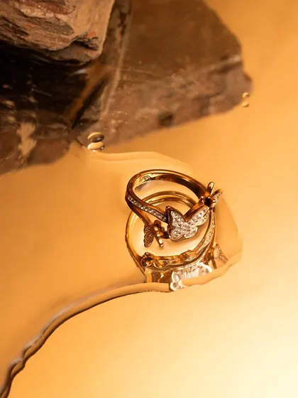 A stunning macro shot of gold butterfly rings in a pool of liquid gold. This image is the definition of luxury, using texture and reflection to create a rich and decadent visual.