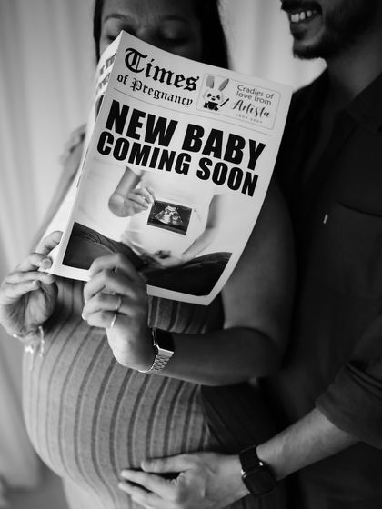 A black and white shot of the couple using the "Times of Pregnancy" newspaper prop. His hand on her bump adds a layer of intimacy to this creative announcement.