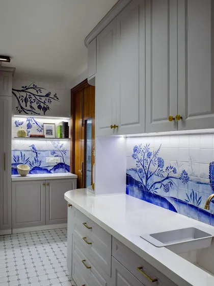 A different angle of the artisanal blue and white kitchen, showing how the mural flows from the backsplash to the wall. The muted grey cabinets provide a calm counterpoint to the detailed tilework.
