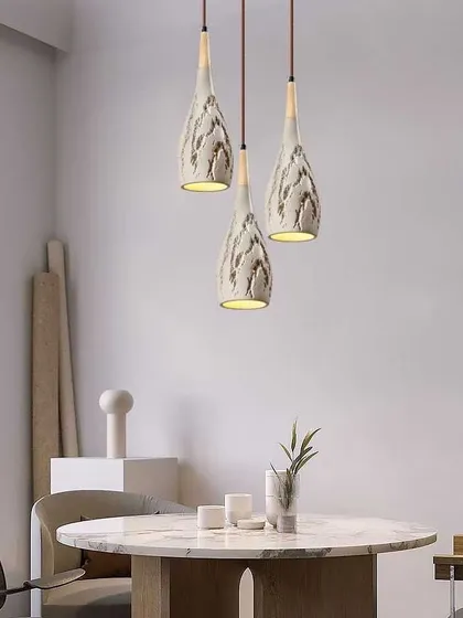 A cluster of three textured ceramic pendants over a dining table. The organic shape and finish add a soft, handmade feel to the space.