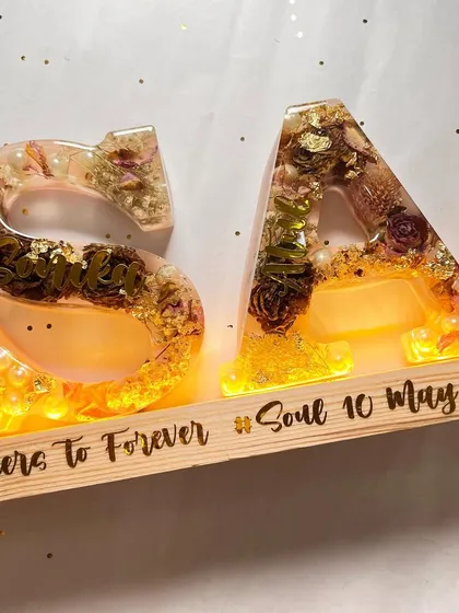 A beautiful shot of the 5.5-inch alphabet lamp with the lights on. The warm light brings out the colors of the preserved flowers and the sparkle of the gold flakes.