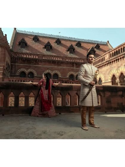 A majestic pre-wedding photograph on the rooftop of a historic building, with the groom standing proudly while his bride looks out from the balcony.