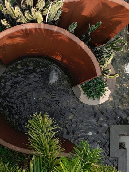 An aerial view of the Corten steel installation at KEUS, showing its fluid, sculptural form wrapping around the water feature. The design provides both privacy and a strong artistic statement.