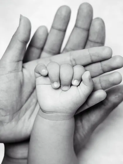 A classic black and white photo of a newborn's hand resting in their parent's palm, a beautiful symbol of their new connection.
