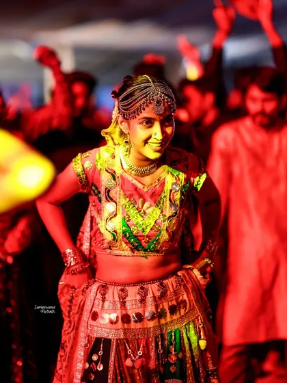 A female dancer is caught in a dramatic red light, her expression a mix of intensity and joy as she moves to the Garba beat.