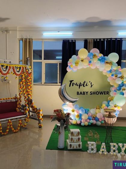 A complete baby shower setup combining a traditional marigold decorated jhula with a modern pastel balloon backdrop.