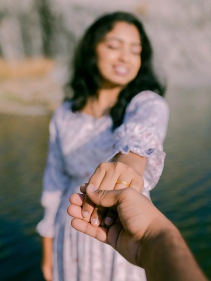 A close-up perspective shot of a couple holding hands, with the focus on their joined hands and the bride's happy expression in the background.