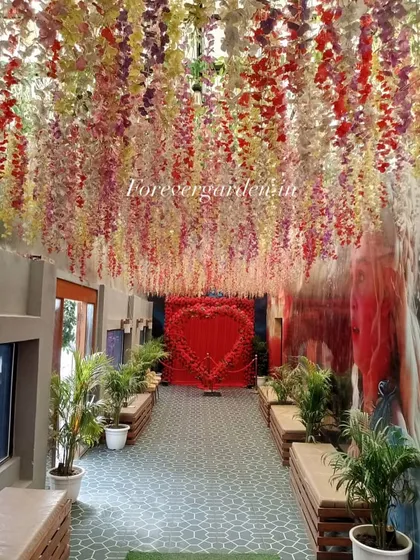 A beautiful wedding or event entrance corridor decorated with hanging wisteria flowers in multiple colors, leading to a heart-shaped floral backdrop.