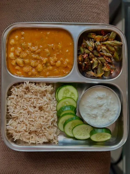 This meal consists of brown rice, channa masala, sautéed ivy gourd, cucumber, and curd. It's a perfect example of a balanced, everyday Indian lunch.