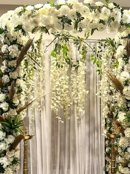 A modern and sophisticated Ganpati decor, this design blends elegant white flowers with trendy dried pampas grass and palm leaves.