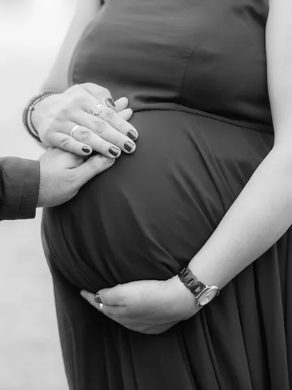 A close-up, black and white shot focusing on the hands of the couple resting on the baby bump, symbolizing protection, love, and connection.