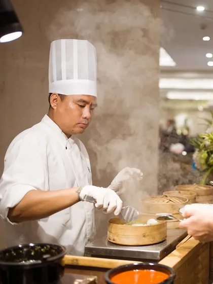A chef carefully tends to steaming bamboo baskets at a live dim sum station. This showcases our commitment to serving fresh, authentic, and skillfully prepared global cuisine with professional care.