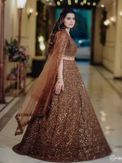A full-length shot of the bride-to-be in her magnificent brown sequined lehenga, capturing her elegance as she looks back over her shoulder.