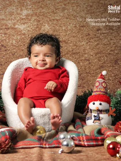 A happy baby in a simple red outfit, ready for his first Christmas portrait next to a friendly snowman prop.