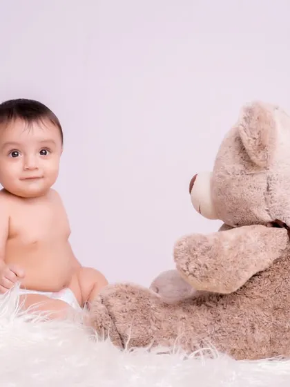 A simple and classic portrait of a baby sitting with a teddy bear on a soft white rug. Sometimes, the simplest setups create the most timeless memories.