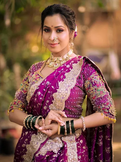 A confident and poised portrait of a model in a traditional Maharashtrian look. The makeup enhances her sharp features and complements the rich purple saree.