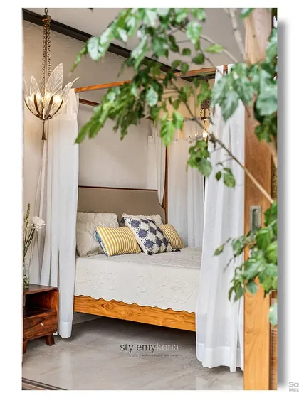 A dreamy four-poster bed draped with soft white curtains, viewed through lush green foliage. This shot, featured in Elle Decor, captures a perfect storybook escape, blending natural elements with romantic design.