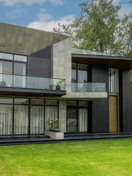 A closer look at the farmhouse project, highlighting the interplay between solid concrete volumes and dark, textured panels. The design emphasizes clean lines, cantilevered balconies, and a strong connection to the green landscape.