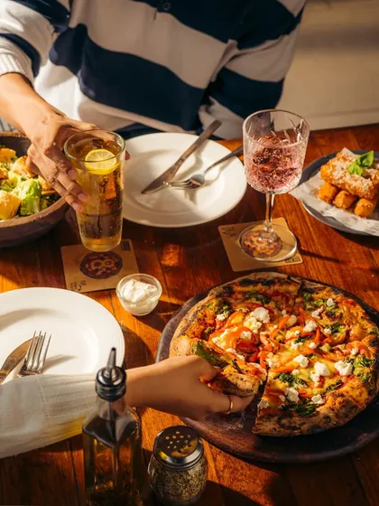 A shared meal is the best meal. Hands reach for slices and drinks, showing how our food brings people together for a good time.