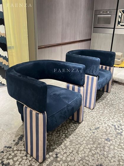 A bold and graphic armchair design. The chair features a deep blue velvet upholstery, a curved back, and distinctive striped block legs, making it a piece of functional art.