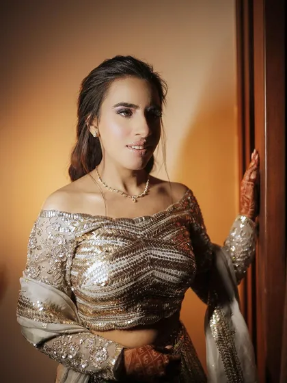 The bride-to-be in her shimmering, off-shoulder engagement lehenga. The intricate sequin work catches the light beautifully, showcasing her glamorous style.