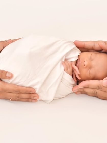 The hands of both parents gently cradle their sleeping newborn, symbolizing protection, love, and unity. This creative shot focuses on the concept of family support.