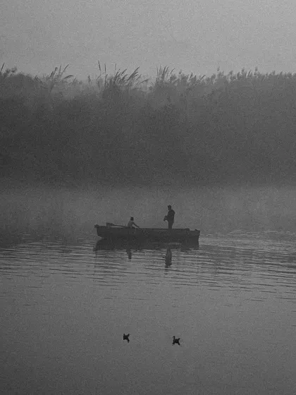 A black and white scene of a boat on the Yamuna river in the early morning fog, creating a minimalist and serene composition.