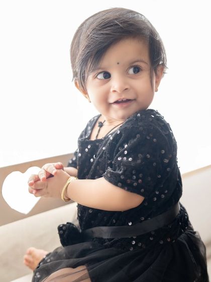 A candid side-profile of a little girl in a black sequin dress, looking off-camera with a sweet expression.