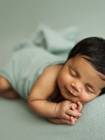 A sweet, sleepy smile. Capturing these little dream-smiles is one of the most rewarding parts of a newborn session. This baby is resting peacefully on a soft mint-green blanket.