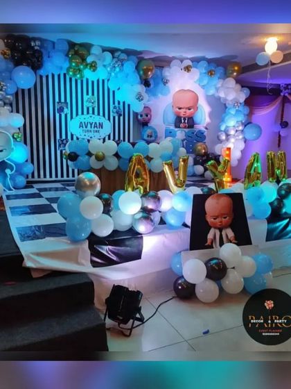 A Boss Baby theme setup on a raised stage. This decoration uses a striped backdrop, a balloon arch, and character props to create a fun and stylish party atmosphere.