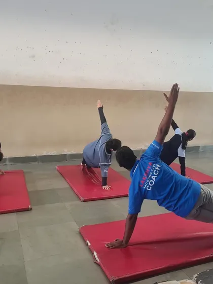 A coach participates in a yoga session alongside athletes, demonstrating the Vasisthasana (side plank pose). My coaches lead by example in all aspects of training.