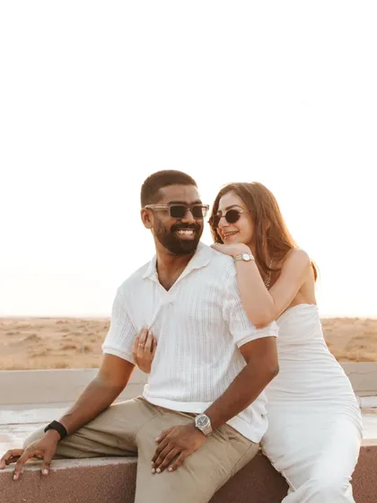 A relaxed and happy portrait of the couple enjoying the sunset. Their coordinated white outfits and genuine smiles make for a timeless and elegant pre-wedding picture.