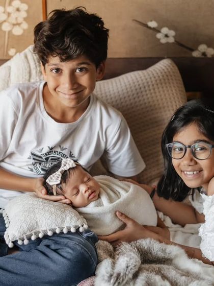 A full house and a full heart. This lifestyle portrait shows older siblings proudly gathered around their new baby sister on the family bed, a beautiful moment of togetherness.