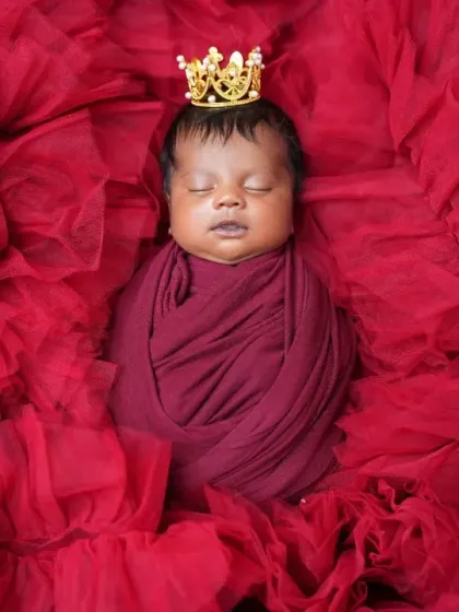 A regal portrait of a newborn wrapped in deep red fabric, wearing a tiny gold crown. The rich color and simple prop create a powerful and majestic image of your little prince or princess.