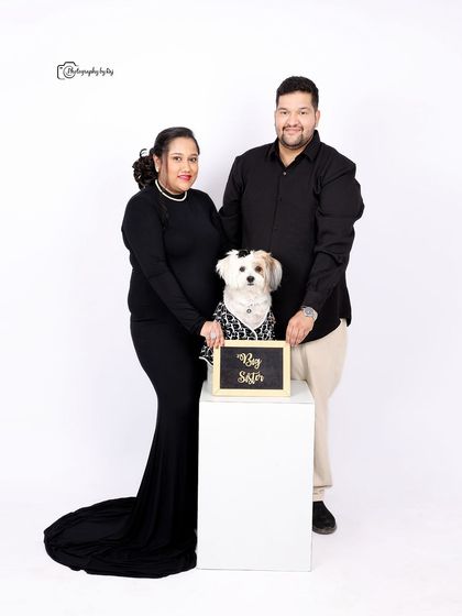 A modern family portrait with a pet. The couple and their stylishly dressed dog pose for a clean, minimalist shot against a white studio background.