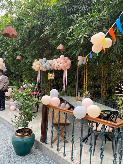 An outdoor party setup at a restaurant with a rustic theme, featuring pastel balloon arrangements and bunting flags.
