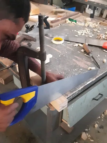 A student from the conventional woodworking batch uses a handsaw and bench hook for a precise cut, a core skill in hand tool training.
