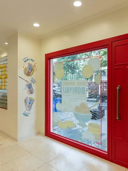 The entrance to the Borivali branch of Parsi Dairy Farm welcomes customers with a bold red door and large glass window. This design choice was intentional to create a sense of invitation and transparency, allowing a peek into the charming world inside.