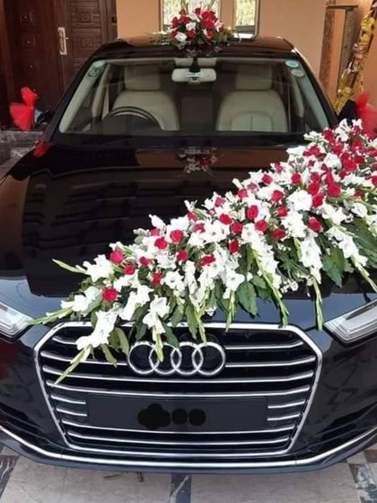 A classic wedding car decoration for a black Audi, featuring a large bouquet of red and white flowers on the hood.