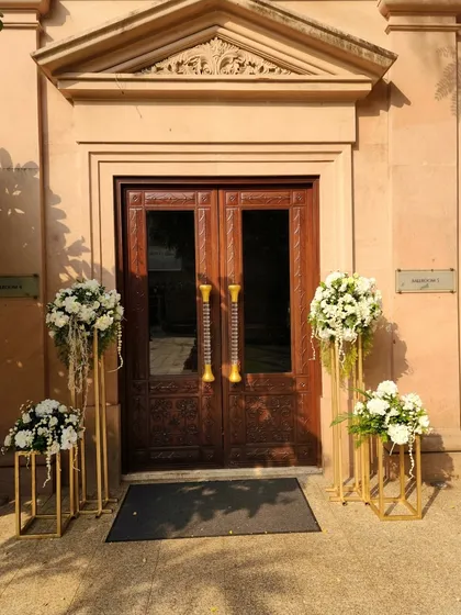 Simple elegance at the entrance of a heritage venue. Tall, slender gold stands hold bouquets of white flowers, framing the beautiful wooden doors without overwhelming the architecture.