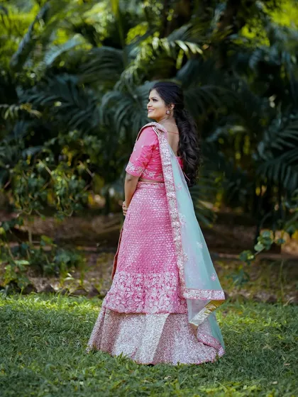 A classic portrait in a lush, green setting. The soft light and natural background bring out the beauty of the woman in her pink lehenga.
