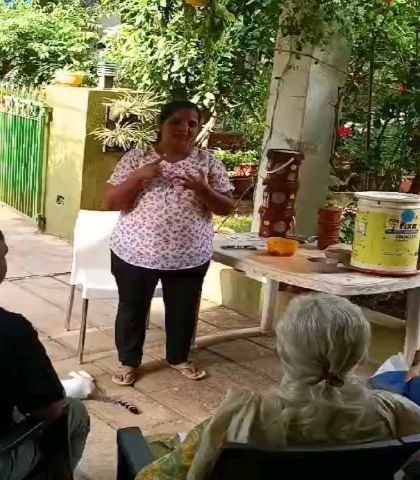 A trainer uses hand gestures to explain the balance of 'greens' (wet waste) and 'browns' (dry material) needed for a healthy compost pile.