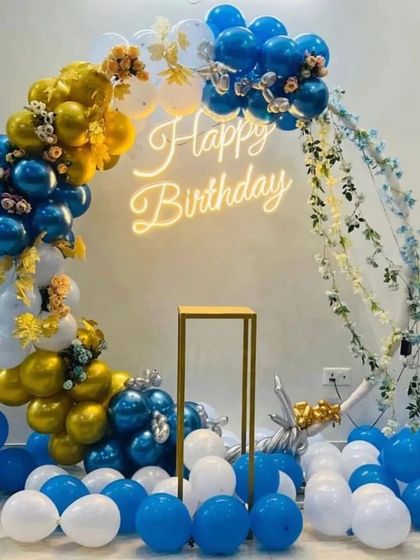 A beautiful circular balloon arch in blue, white, and gold, complete with a 'Happy Birthday' neon sign. This versatile piece can serve as a stunning backdrop for photos or a cake table.